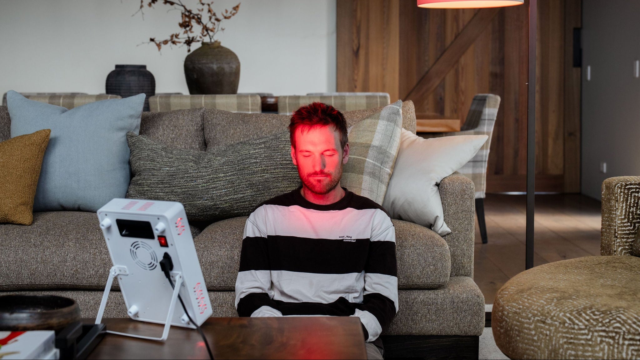 Person sitting on a couch with a device emitting red light in a living room setting.